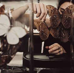 a woman sitting at a table with two butterflies on her hands and another butterfly in the background