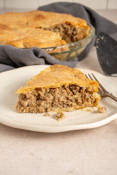 a piece of meat pie on a plate with a fork next to the rest of the pie