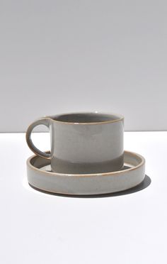 a gray cup and saucer sitting on top of a white countertop next to each other