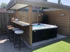 an outdoor hot tub with bar stools in the back ground and wooden fence around it