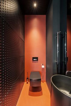 a modern bathroom with an orange floor and black walls, along with a large round sink