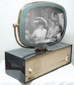 an old tv sitting on top of a wooden box with two people in the background