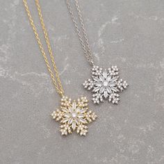 two snowflake necklaces sitting on top of a stone surface, one is gold and the other is silver