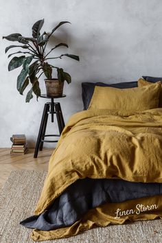 a bed with yellow linens and pillows in a white room next to a potted plant