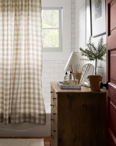 a bathroom with a checkered shower curtain and wooden dresser in front of the window