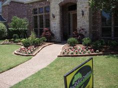 a sign in front of a brick house with landscaping around it and flowers on the lawn