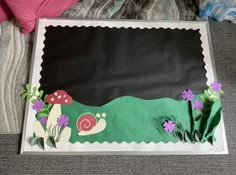 a sheet cake that is shaped like a snail and grass with flowers on the bottom