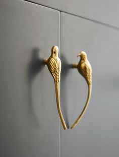 two gold bird hooks on the side of a gray wall