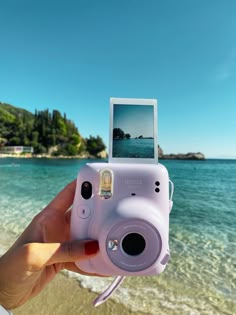 a person holding up a camera in front of the ocean with an island in the background