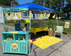 a lemonade stand is set up in front of a white house with blue awnings