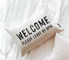 two pillows sitting on top of a bed with the words welcome and please leave by 9pm