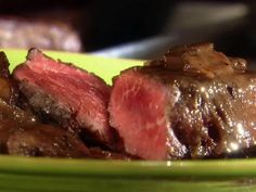 a green plate topped with sliced up steak on top of it's side next to a fork