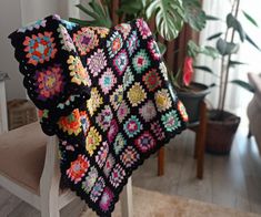 a crocheted blanket sitting on top of a wooden chair next to a potted plant