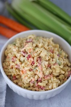 a white bowl filled with macaroni salad next to carrots and celery