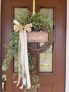 a welcome sign hanging on the front door with a wreath and ribbon tied around it