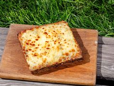 a square piece of cheese bread on a wooden cutting board with grass in the background