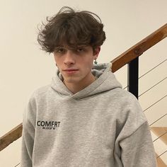 a young man wearing a grey sweatshirt standing in front of stairs