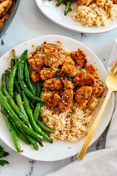 two plates with rice, green beans and chicken on them next to some silverware