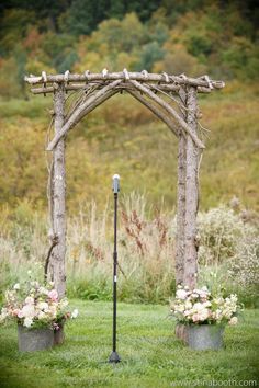 an arch made out of branches with flowers in buckets