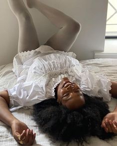 a woman laying on top of a bed wearing a white dress and gold jewelry with her legs spread out