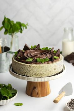 a cake with chocolate frosting and mint sprigs sits on a wooden stand