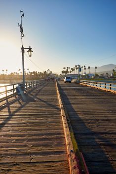 the sun is shining on a pier with cars driving along it and palm trees in the background