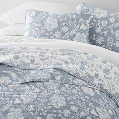 a bed with blue and white floral comforter set on it's headboard