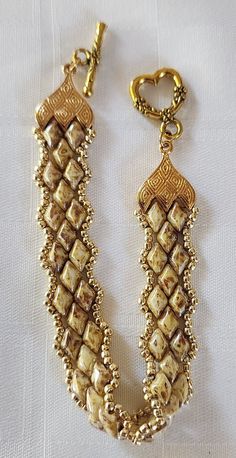 a gold and white beaded bracelet on a white tablecloth with a golden clasp