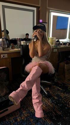 a woman sitting on top of a chair while holding a microphone to her ear and wearing pink boots