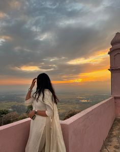 a woman standing on top of a pink wall next to a tall tower with a sunset in the background