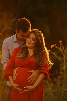 a pregnant woman in a red dress standing next to a man with his hands on her belly