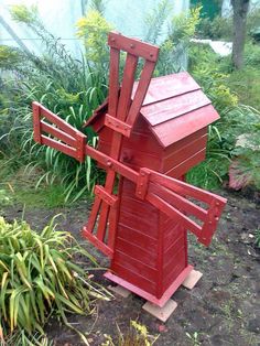 a red wooden windmill sitting in the middle of a garden