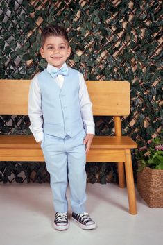 a young boy wearing a blue suit and bow tie standing in front of a wooden bench