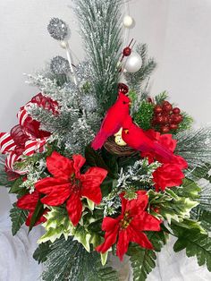 a red bird sitting on top of a vase filled with poinsettias and greenery