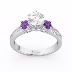 a white gold ring with three purple stones on the band and an oval center stone