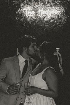 a man and woman kissing in front of a neon sign that says the hog on it