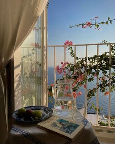 an open window overlooking the ocean with fruit on a plate and book next to it