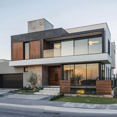 a modern house with lots of windows and wood accents on the front door, along with two garages