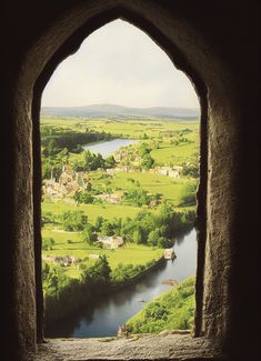 an arched window with a view of a river running through the middle of a lush green countryside