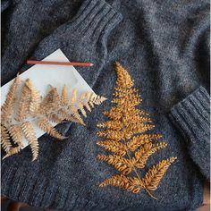 a sweater with some plants on it next to a pencil and an object in the background