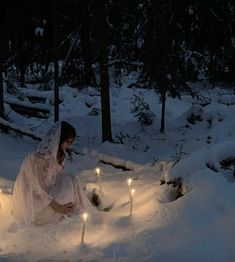 a woman kneeling in the snow next to candles