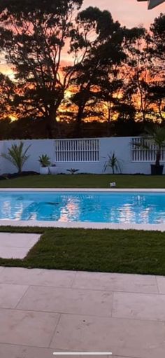 an empty swimming pool with grass and trees in the background at sunset or sunrise time