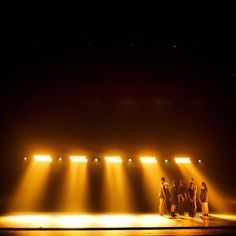 three people standing on a stage in front of spotlights with their backs turned to the side