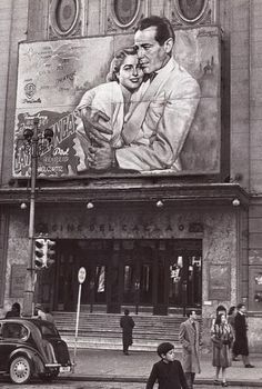 an old black and white photo of people walking in front of a building with a large painting on it's side