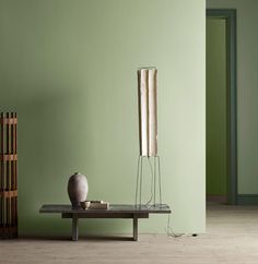 a table with a vase on it in front of a green wall and a wooden shelf