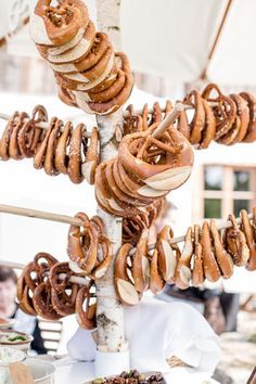 an assortment of pretzels hanging from a tree at a food stand with people in the background