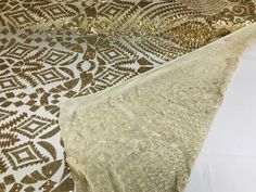 two pieces of gold sequins and fabric on a white tablecloth with brown designs