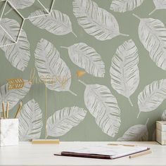 a desk with a book, pen and notebook on it in front of a wallpapered background