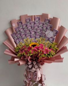 a vase filled with lots of pink and yellow flowers next to a pile of money