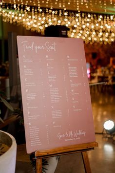 a pink wedding seating plan on a wooden easel in front of a chandelier